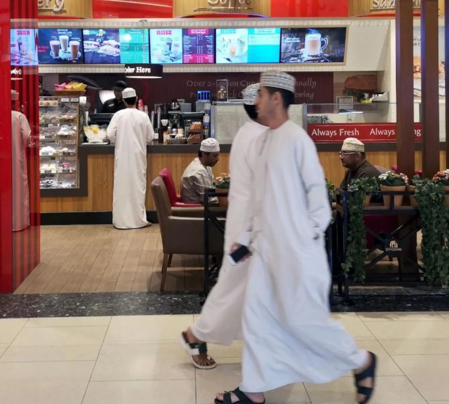 رجلان يمران  أمام أحد المقاهي في مسقط (رويترز)