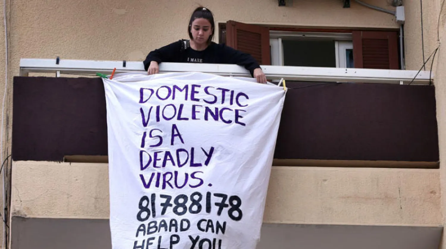 لبنانية تطل من شرفتها أثناء الحجر وتحمل لافتة كتب عليها «العنف الأسري فيروس مميت» مع رقم جمعية أهلية تقدم المساعدة (أ.ب)