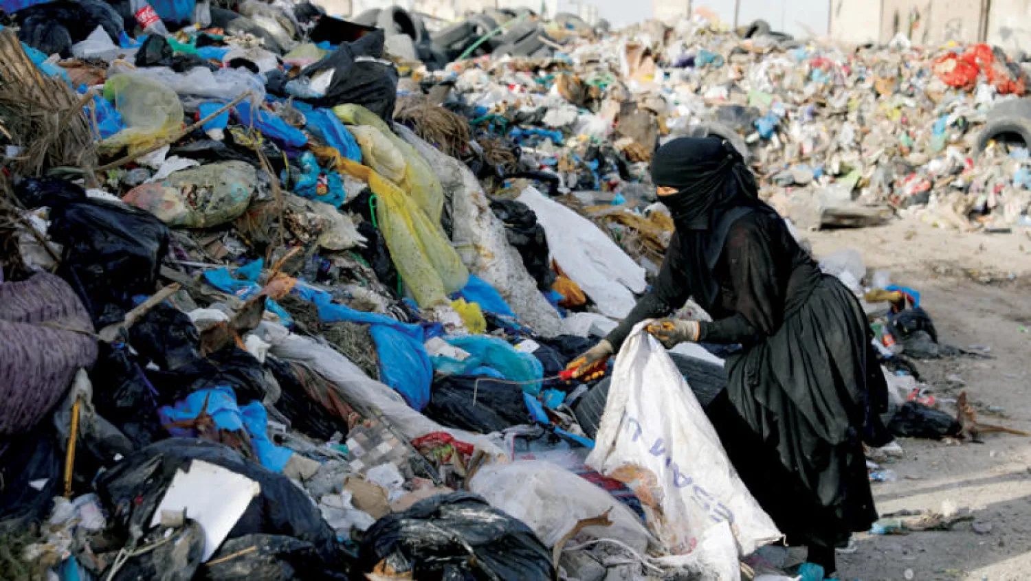 عراقية تبحث عن مواد قابلة للتدوير في كومة قمامة ببغداد أمس (رويترز)