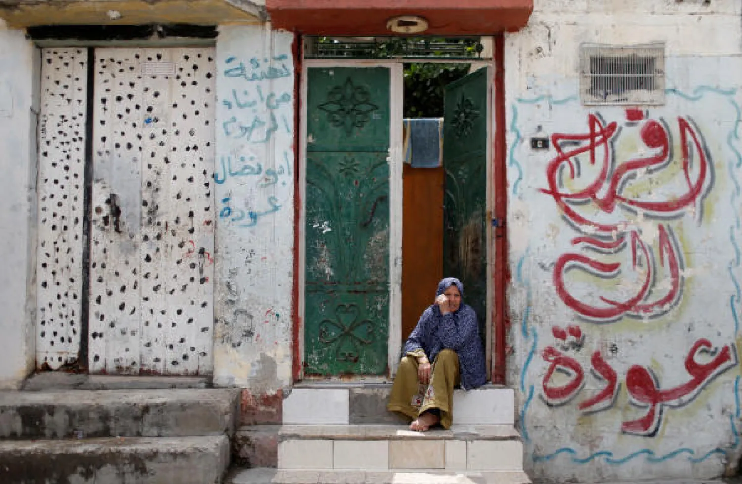 سيدة تجلس خارج بيتها في مخيم جباليا بقطاع غزة (رويترز)