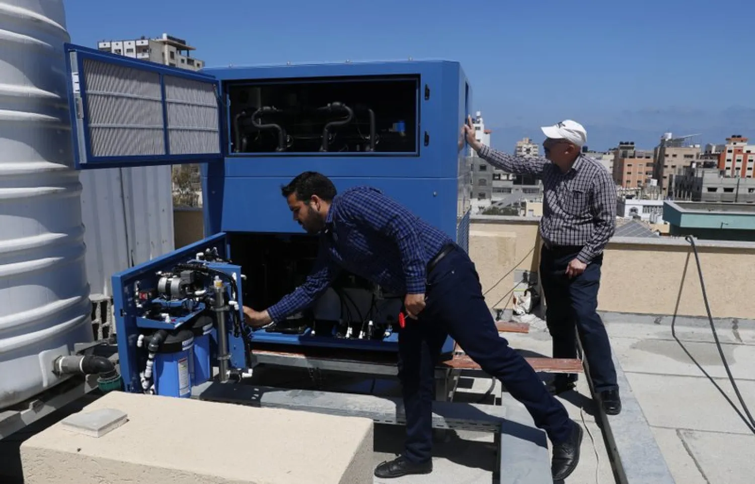 In this Thursday, April 30, 2020 photo, Palestinian engineer Raed Nakhal from Palestine Children Relief Fund, right, and engineer Abdullah Dewik, check the GEN-M machine that generates safe drinking water from air at the roof of al-Rantisi pediatric hospital in Gaza City. (AP Photo/Adel Hana)