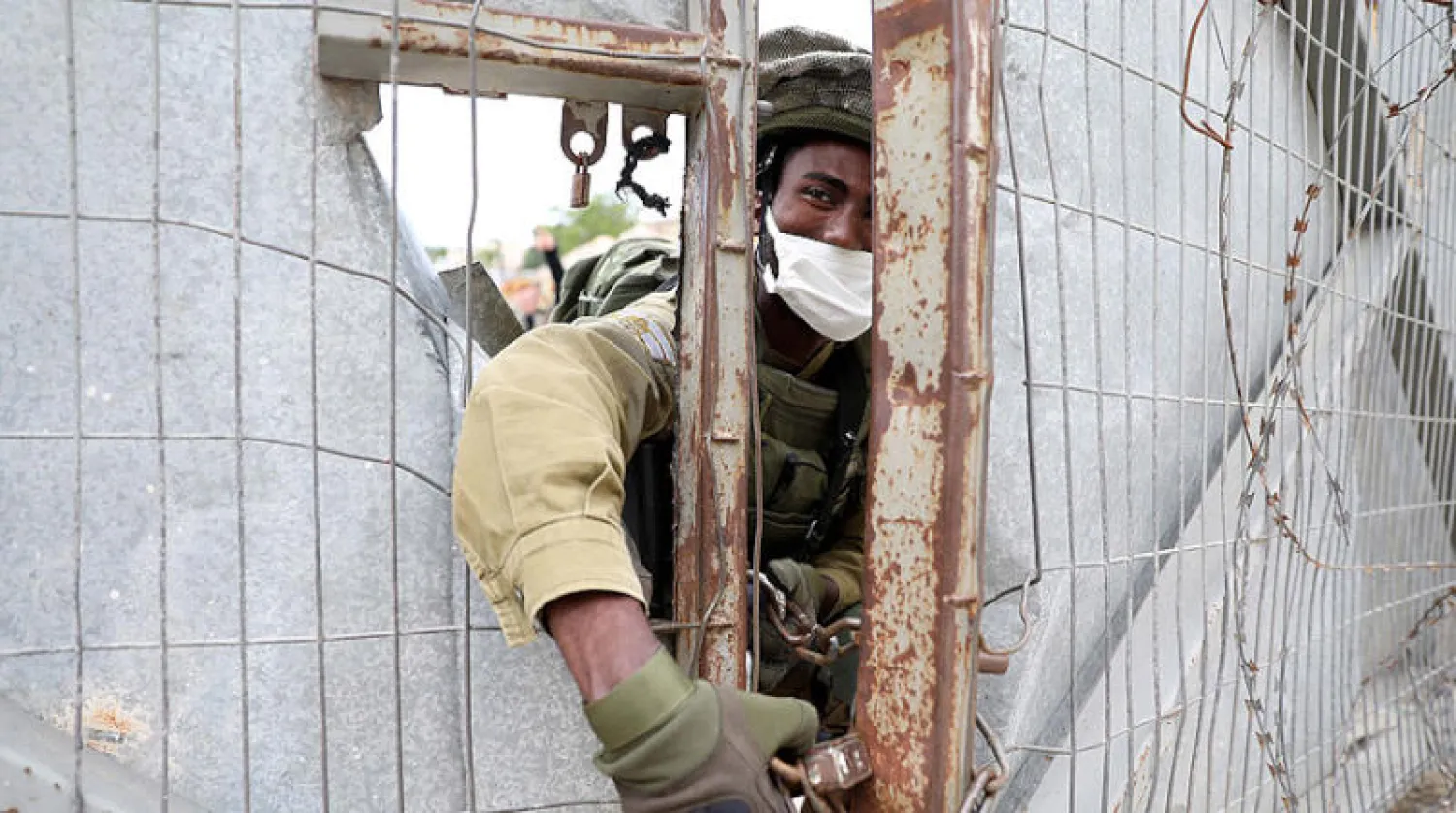 جنود إسرائيليون يفتحون قفل بوابة في الخليل بالضفة للسماح بمرور مستوطنين (إ.ب.أ)