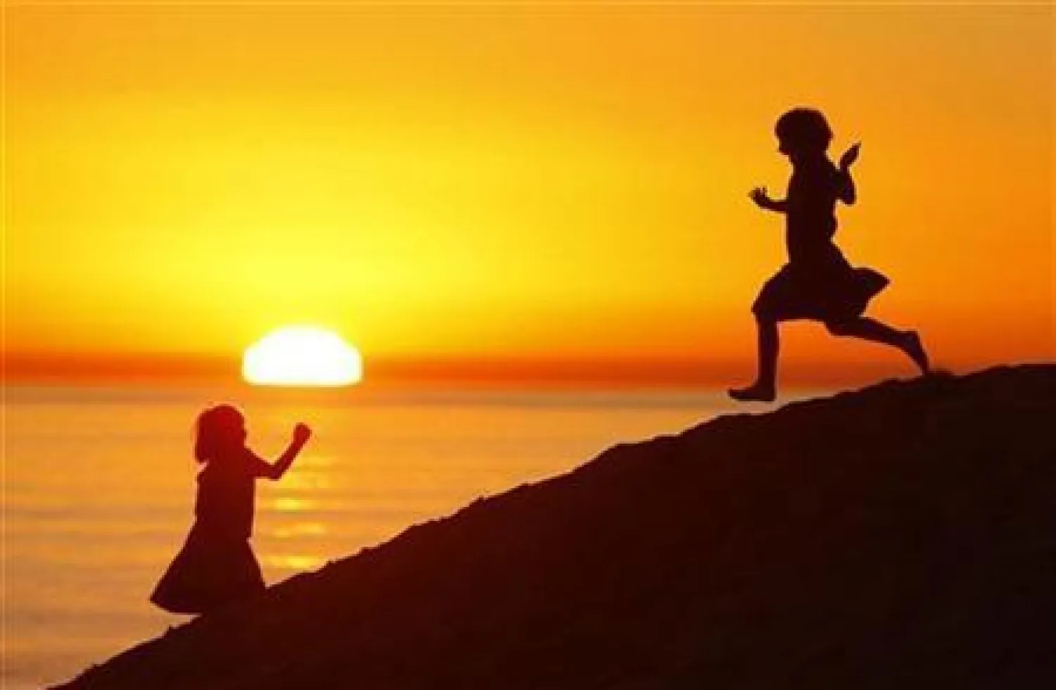 فتاتان تلعبان بالقرب من احد شواطىء كاليفورنيا ويظهر غروب الشمس خلفهما (أرشيف - رويترز)