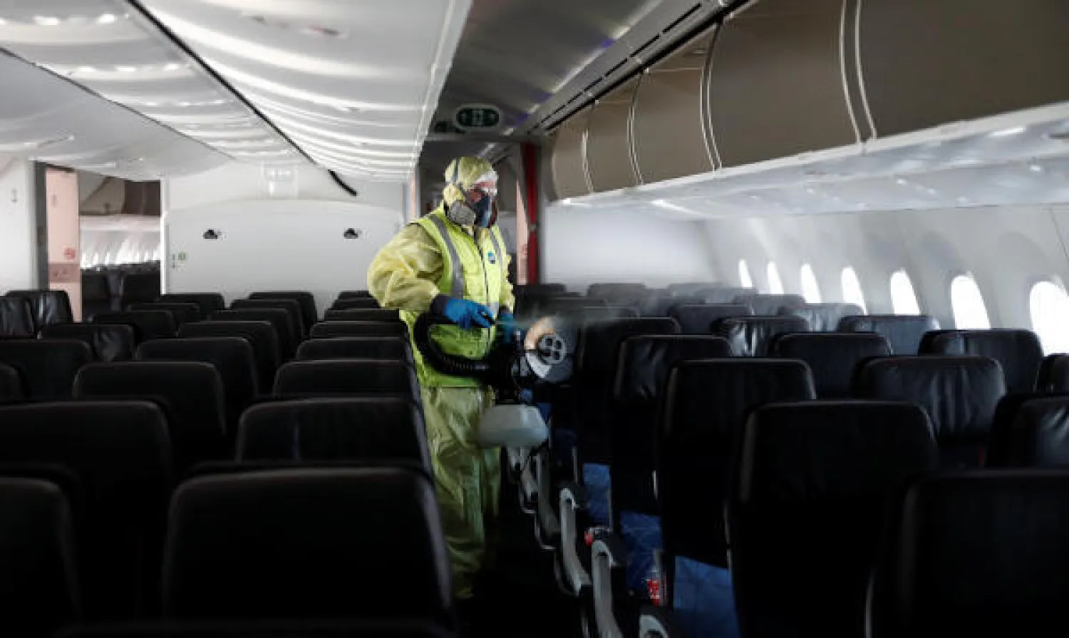 عامل يرتدي بدلة واقية يعقّم طائرة من طراز «بوينغ 787» (رويترز)