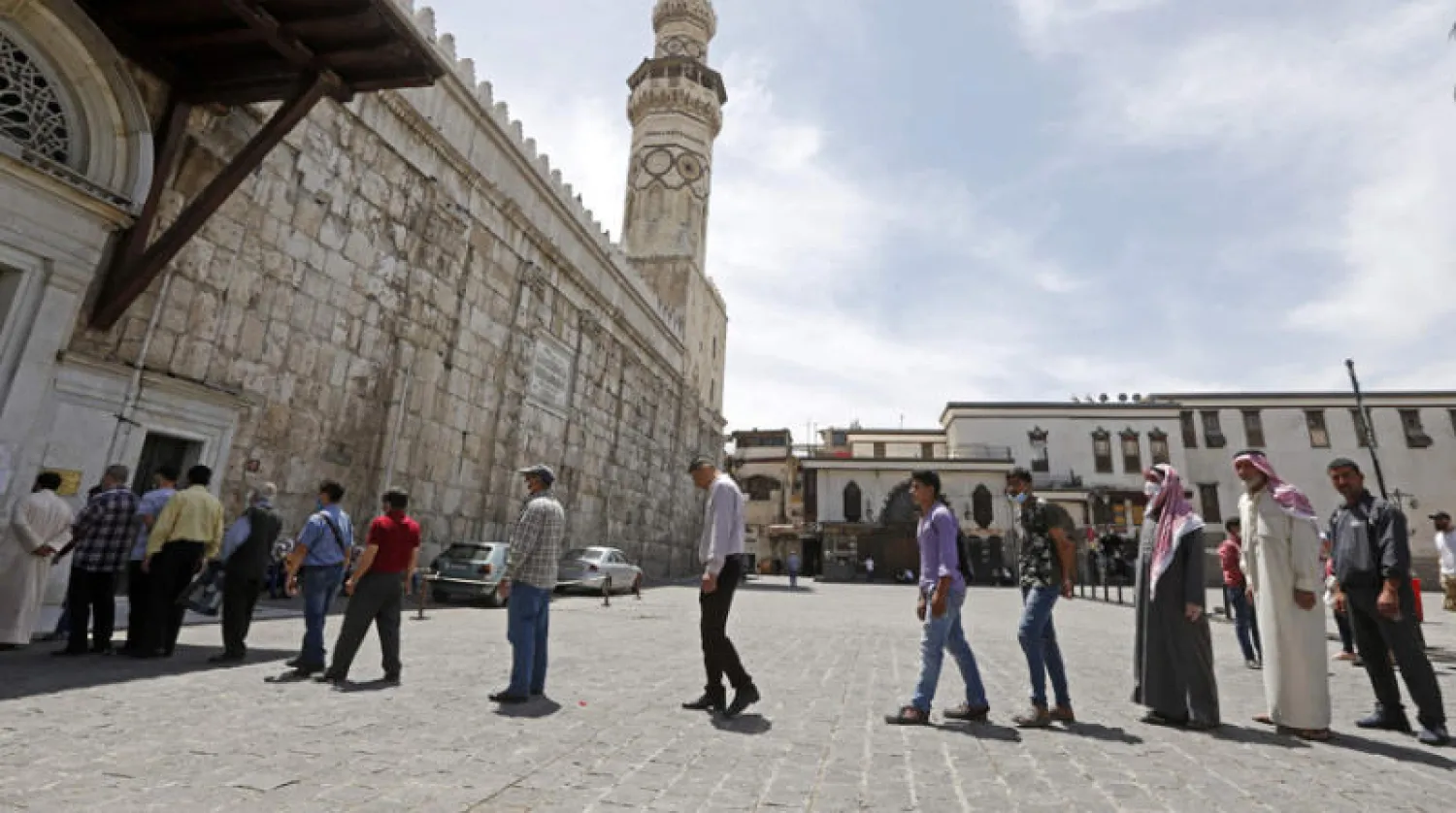 مصلون يرتدي بعضهم كمامات واقية من «كورونا» يقفون في طابور لدخول الجامع الأموي بدمشق أمس (أ.ف.ب)