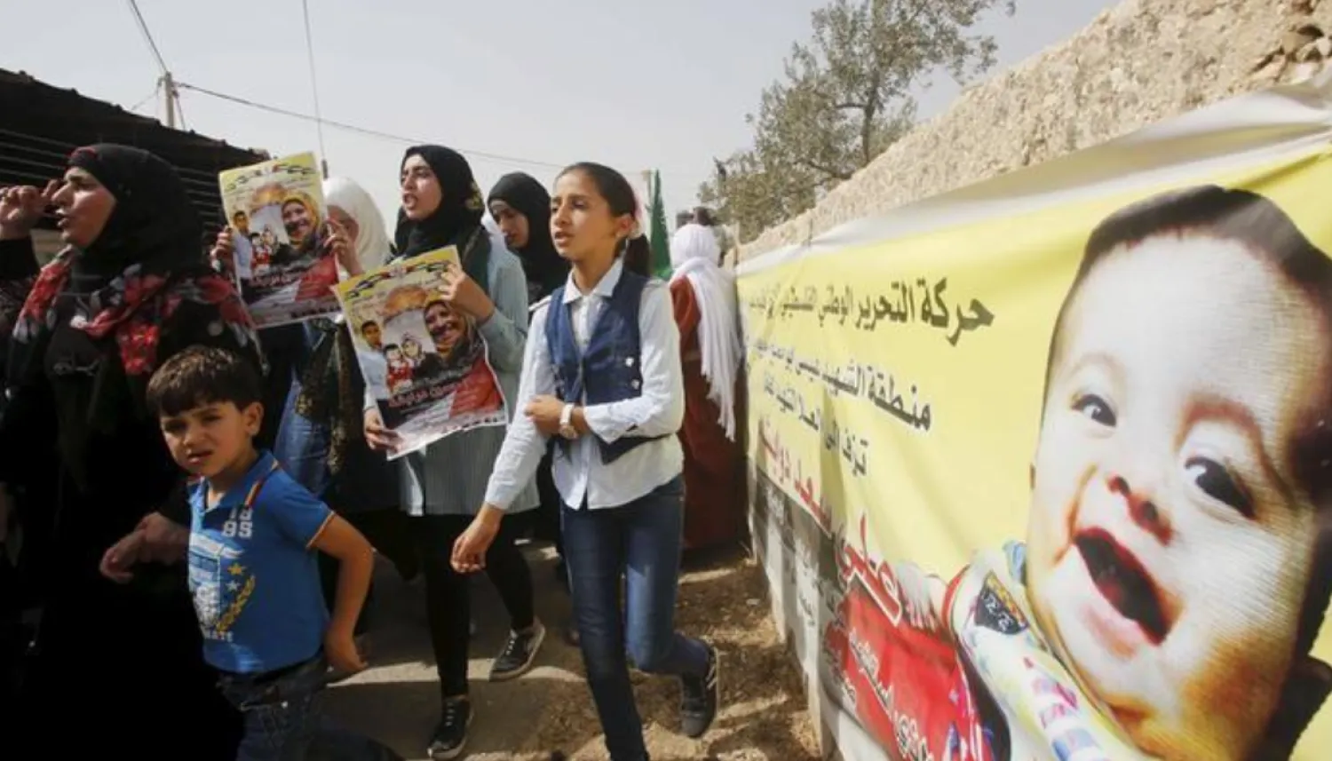 Mourners hold posters of Palestinian Riham Dawabsheh, 27 and her family as they walk past a banner depicting her 18-month-old son Ali during her funeral at Duma village near the occupied West Bank city of Nablus, September 7, 2015. REUTERS/Abed Omar Qusini/Files
