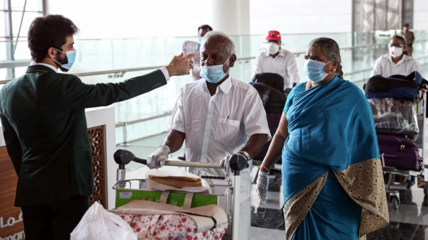 Indian nationals residing in Oman, wearing face masks due to the COVID-19 coronavirus pandemic, have their body temperatures measured at a terminal in Muscat International Airport ahead of their repatriation flight from the Omani capital, on May 12, 2020. (Photo by MOHAMMED MAHJOUB / AFP)