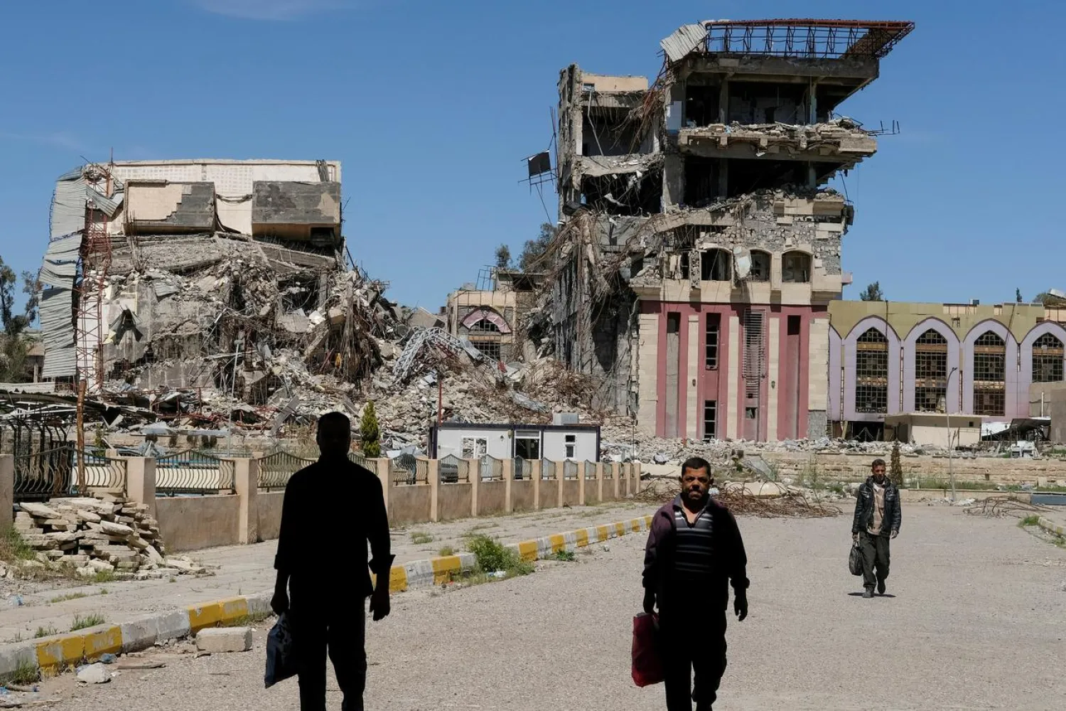 People walk in front of the remains of the University of Mosul, which was burned and destroyed during a battle with ISIS militants, in Mosul, Iraq, April 10, 2017. REUTERS/Marko Djurica/File photo