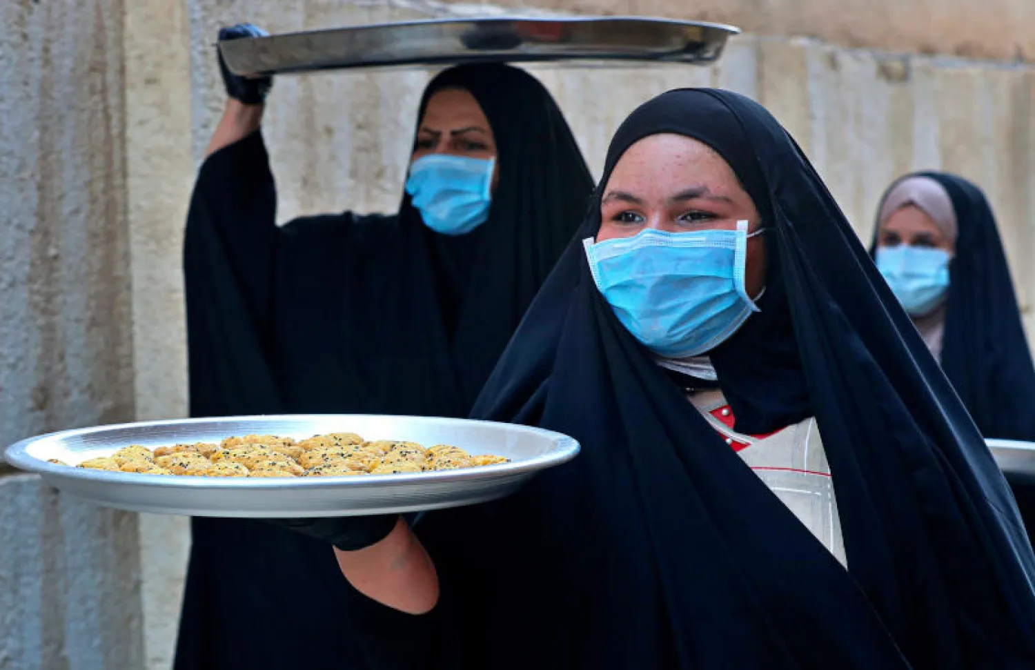 سيدات يرتدين كمامات في البصرة وهن يحملن حلوى عيد الفطر (أ.ب)