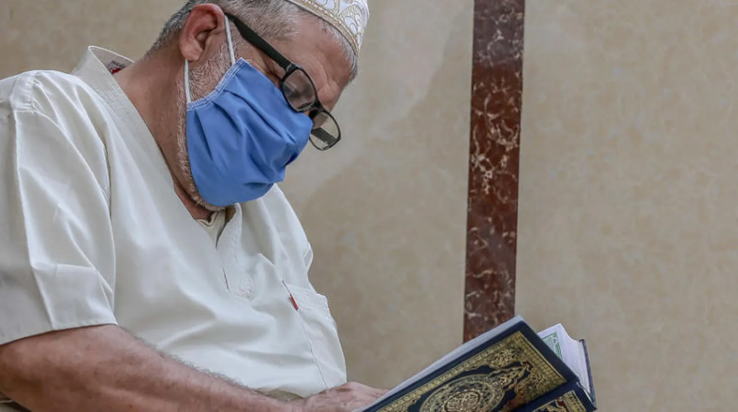فلسطيني يضع كمامة ويقرأ القرآن الكريم يوم الجمعة في مسجد بمدينة غزة في قطاع غزة الذي سجّل أمس أول وفاة بفيروس كورونا (إ.ب.أ)