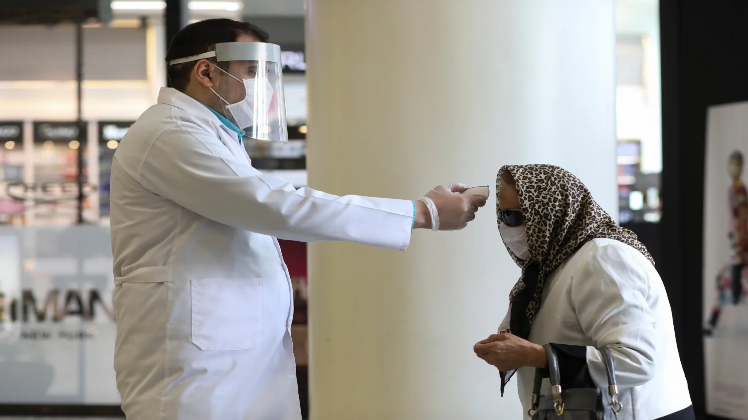 A man wears a face mask and a protective face shield as he checks a woman's temperature, to let her go inside the mall, following the outbreak of the coronavirus, after shopping malls and bazaars reopened in Tehran, Iran, April 20, 2020. Photo by WANA (West Asia News Agency)/Ali Khara via Reuters

