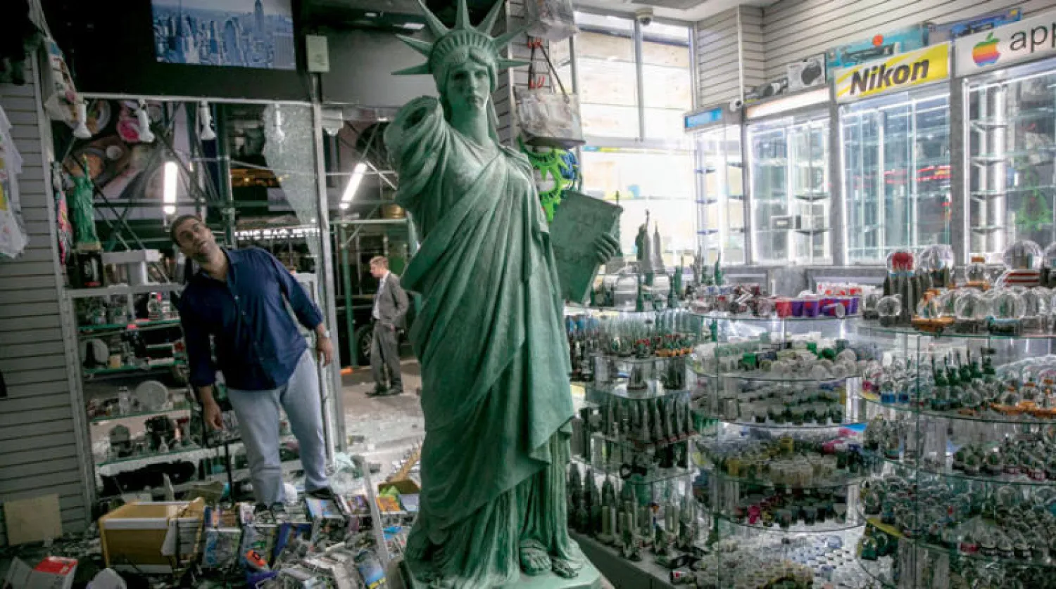 صاحب متجر في نيويورك يعاين أمس الدمار الذي لحق بمتجره الليلة قبل الماضية (أ.ف.ب)