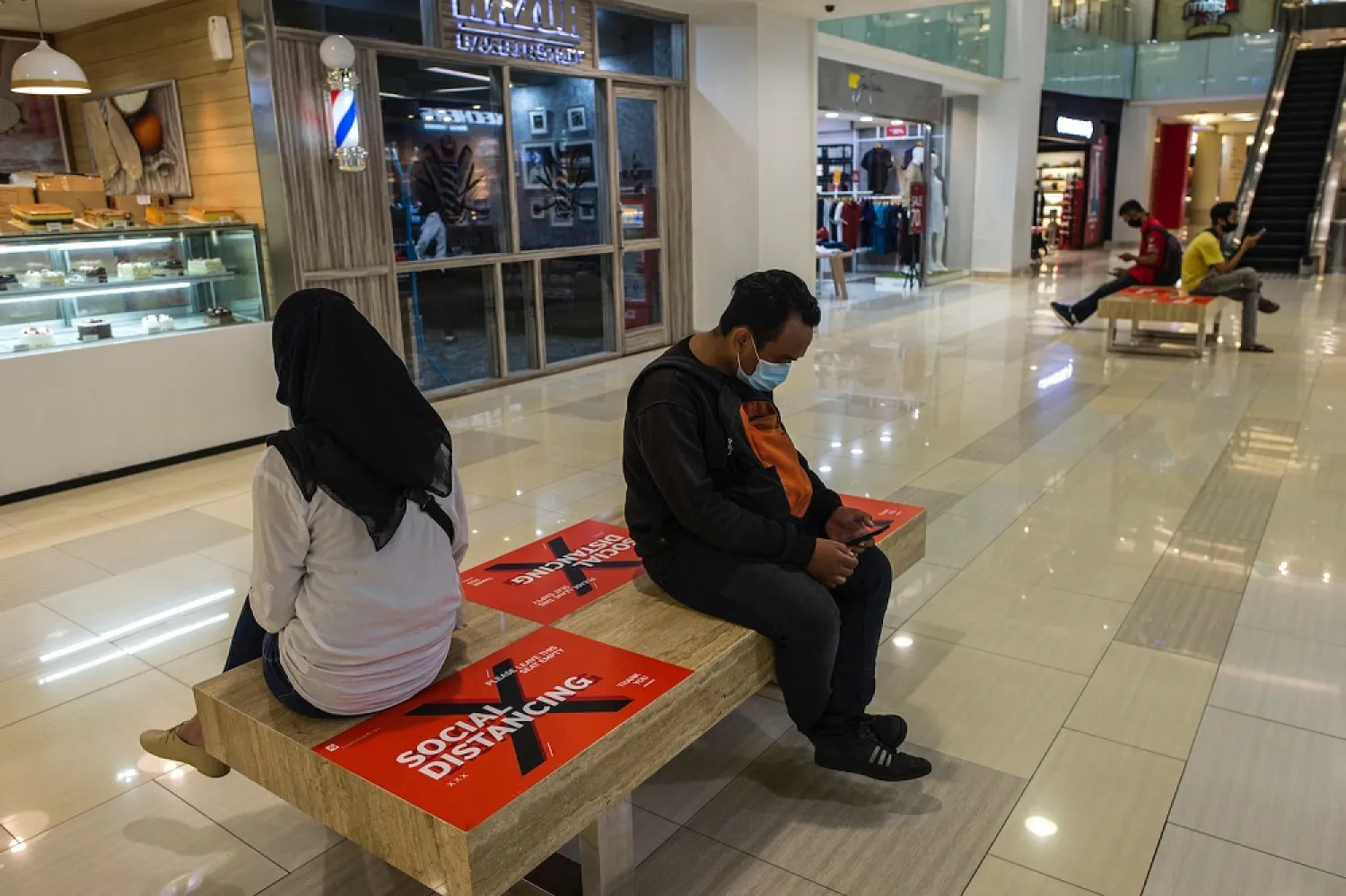 People sit on benches with sections marked off for social distancing at a mall in Surabaya, Indonesia, on April 20, amid the coronavirus pandemic. (AFP)