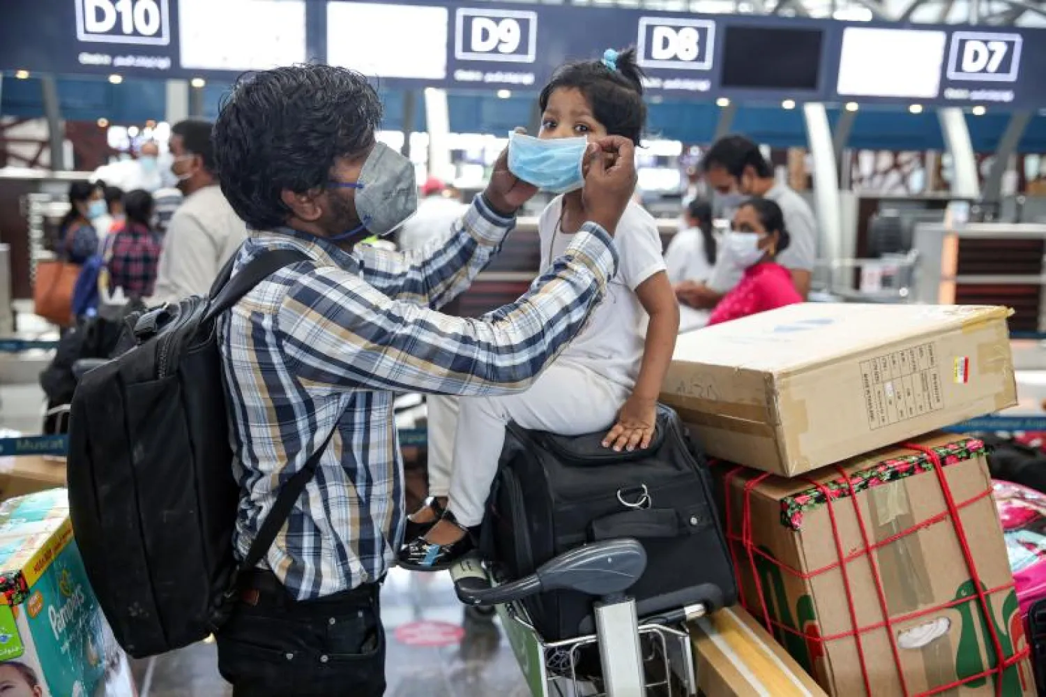 أب هندي يساعد ابنته على ارتداء الكمامة في مطار مسقط الدولي استعداداً للعودة إلى بلدهما (أ.ف.ب)