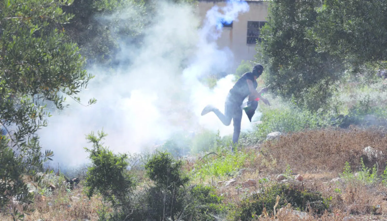 فلسطيني يعيد رمي غاز مسيل للدموع أطلقه الجيش الإسرائيلي قرب نابلس الجمعة (إ.ب.أ)