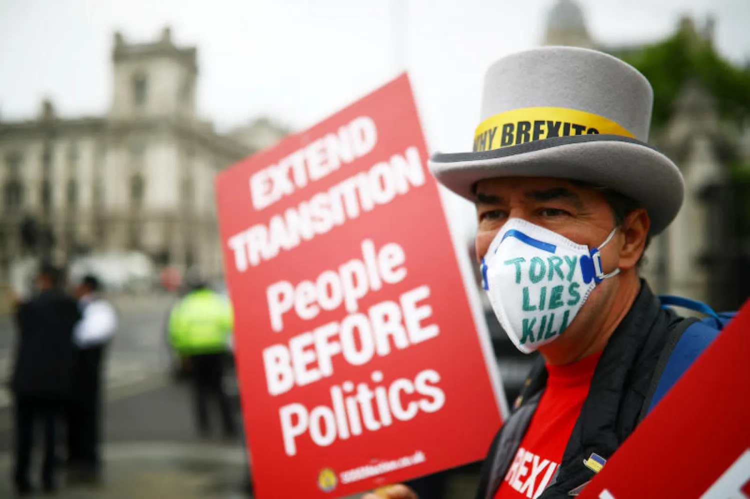 رجل يتظاهر في لندن حاملًا شعار «الناس قبل السياسة» (رويترز)
