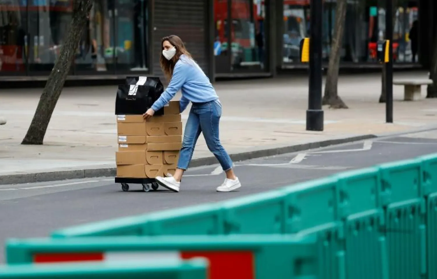 عاملة في مجال البيع بالتجزئة تضع كمامة فيما تقوم بنقل صناديق بشارع أوكسفورد في لندن (أ.ف.ب)