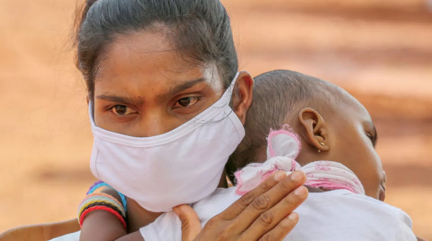 أم وطفلها ينتظران العودة إلى بلدتهما بعد تخفيف إجراءات {كورونا} في سريلانكا (إ.ب.أ)