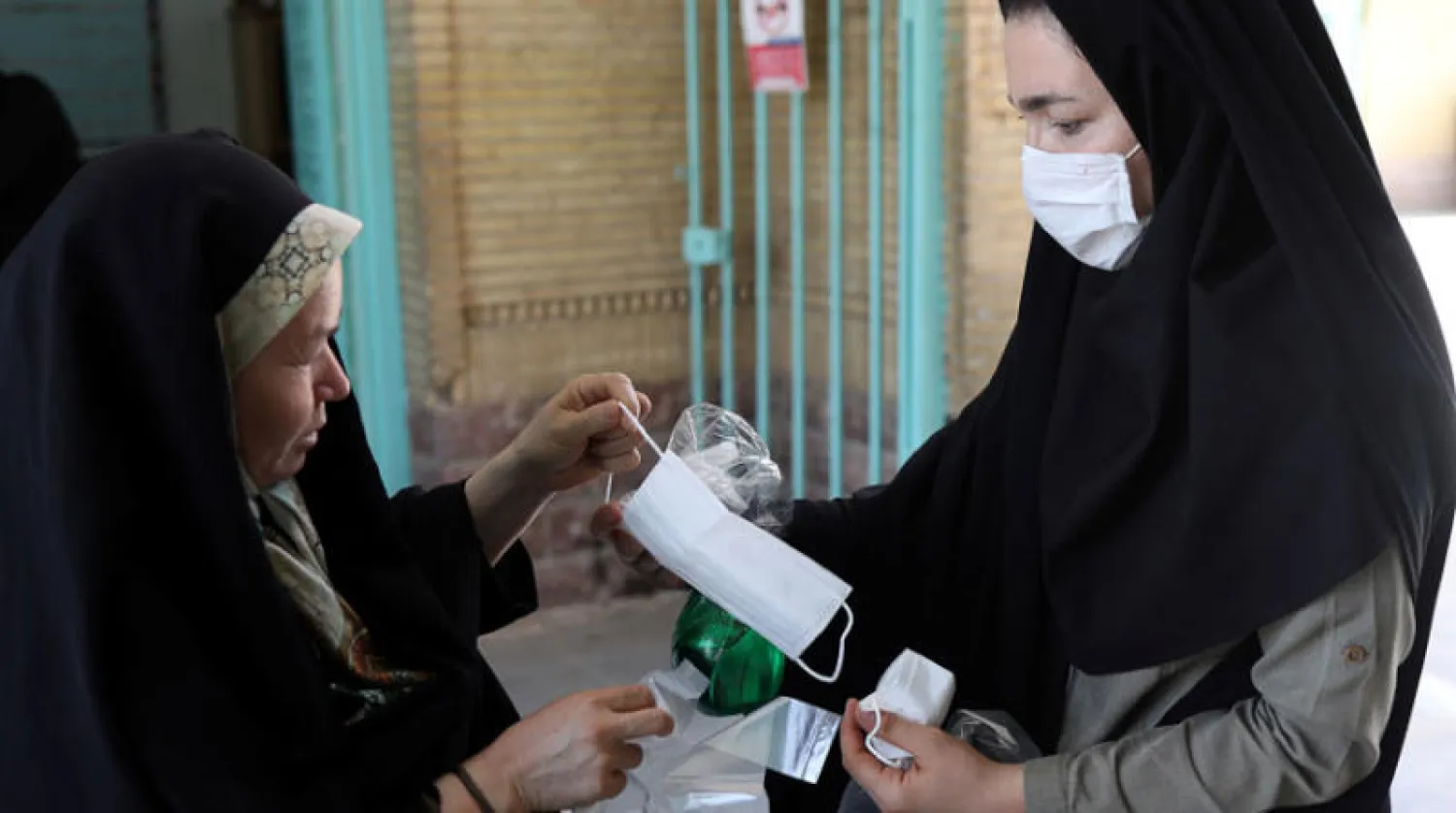 سيدة إيرانية توزع كمامات عند مدخل مسجد في ضواحي طهران الجمعة (رويترز)