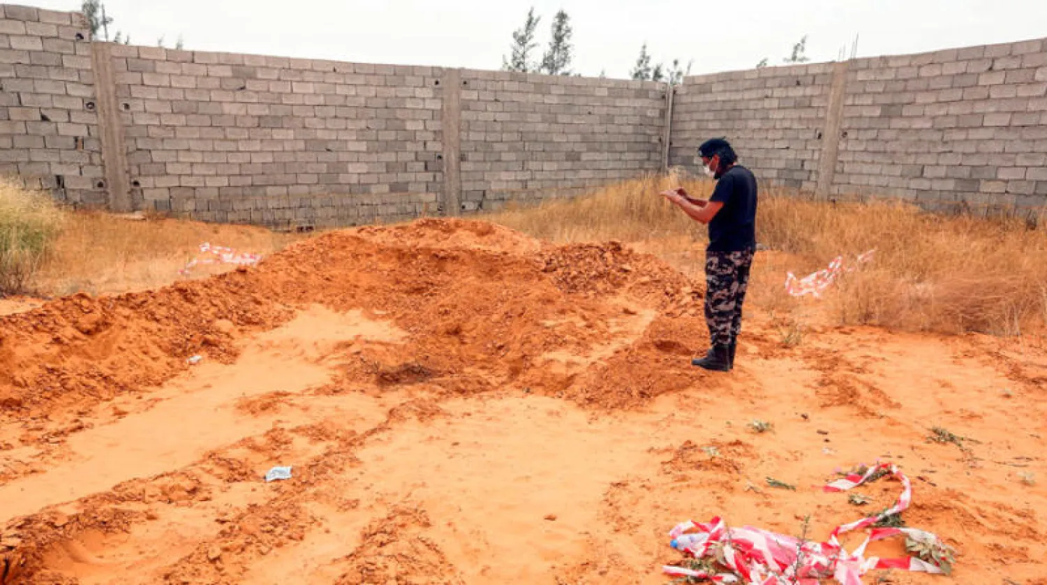 أحد عناصر القوات الموالية لحكومة {الوفاق} يقف وسط قبر جماعي عُثر عليه في ترهونة (أ.ف.ب)