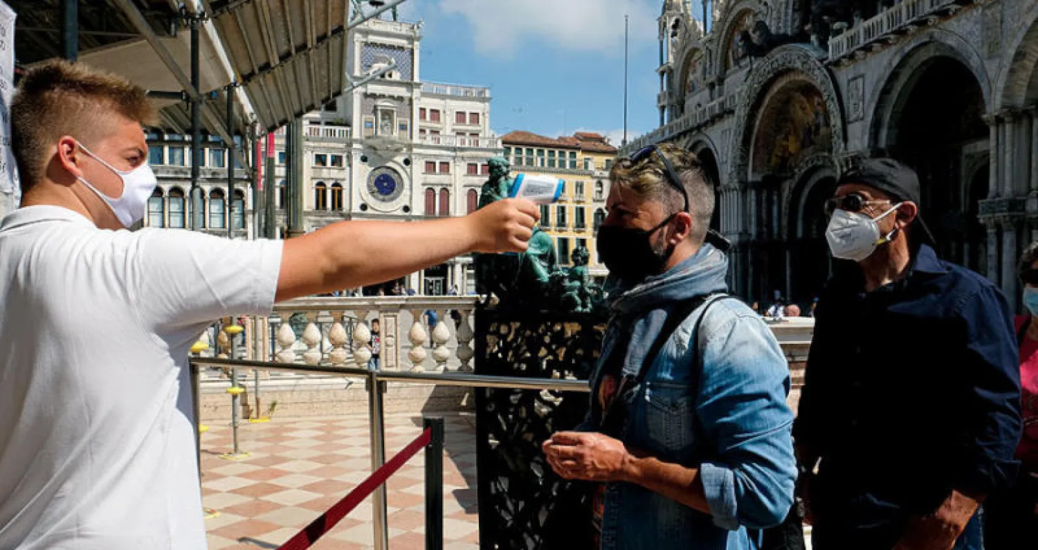 موظف يقيس درجة حرارة سائحة في مدخل برج «سانت مارك» بمدينة البندقية أمس (رويترز)