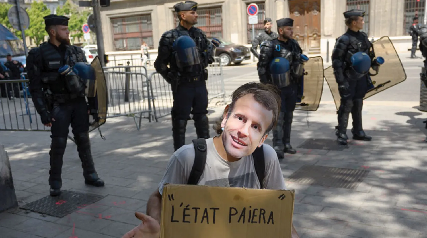 أحد عاملي القطاع الصحي يرتدي قناع وجه الرئيس إيمانويل ماكرون خلال مظاهرة في باريس أمس (أ.ف.ب)