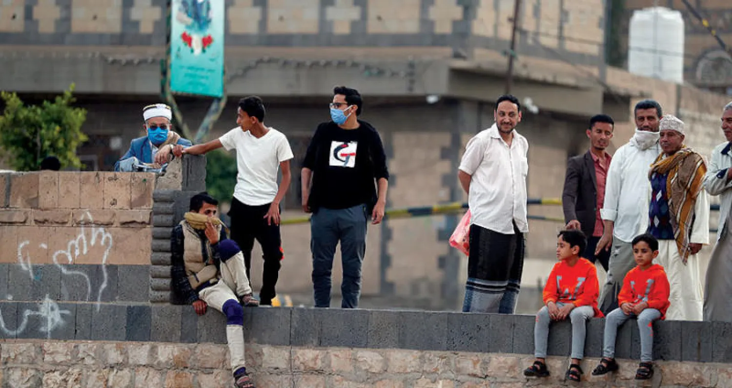 الملصقات تتوزع في أنحاء صنعاء كما يبدو ملصق لأحد القتلى وراء يمنيين يتفرجون على مباراة كرة قدم للهواة وسط صنعاء (إ.ب.أ)