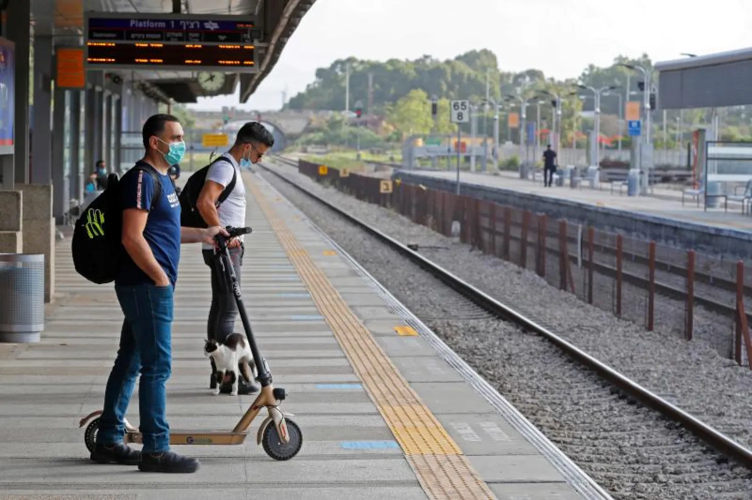 رجلان يرتديان قناعي وجه خوفاً من فيروس كورونا أثناء إنتظارهما القطار في إسرائيل (أ.ف.ب)