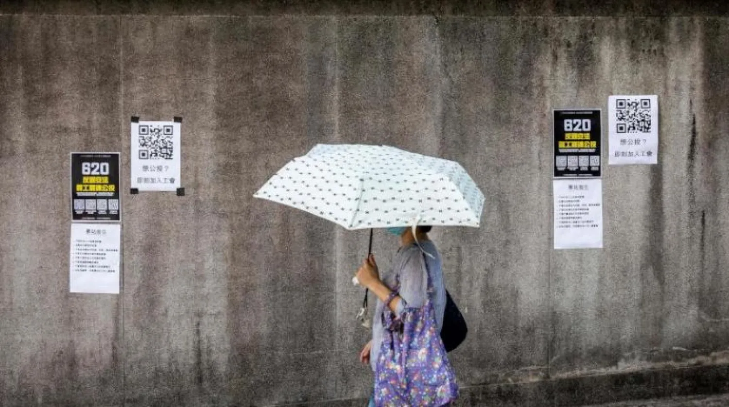Bir kadın Hong Kong'da  Ulusal Güvenlik Yasasını reddeden pankartların önünden geçiyor (AFP)
