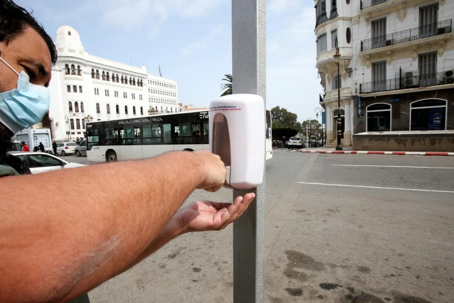 FILE PHOTO: A man wearing a protective face mask uses a hand sanitizer dispenser on the street following the spread of the coronavirus, in Algiers, Algeria March 21, 2020. REUTERS/Ramzi Boudina