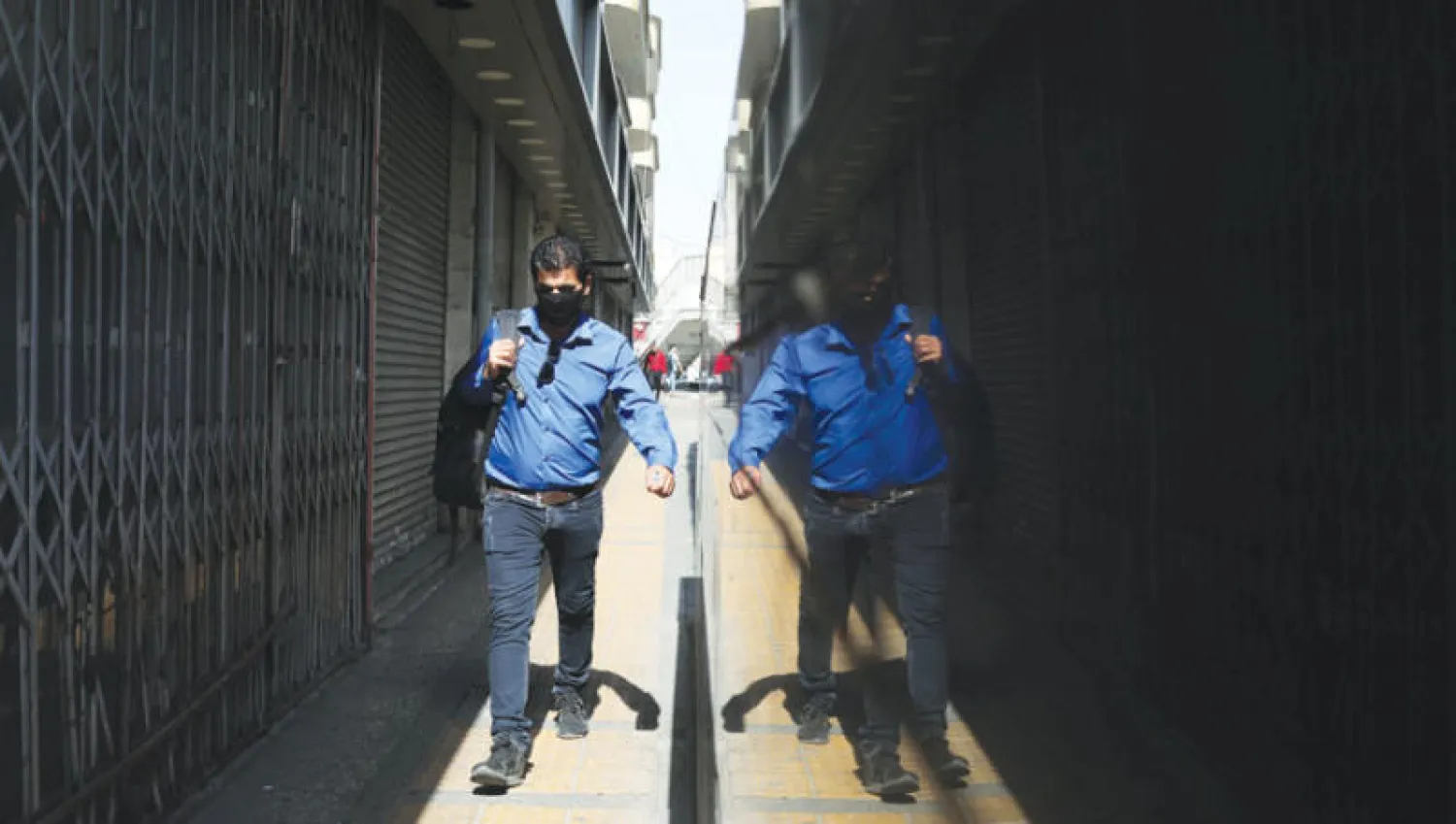 إيراني يرتدي كمامة للوقاية من فيروس «كوفيد - 19» في زقاق وسط طهران أول من أمس (رويترز)