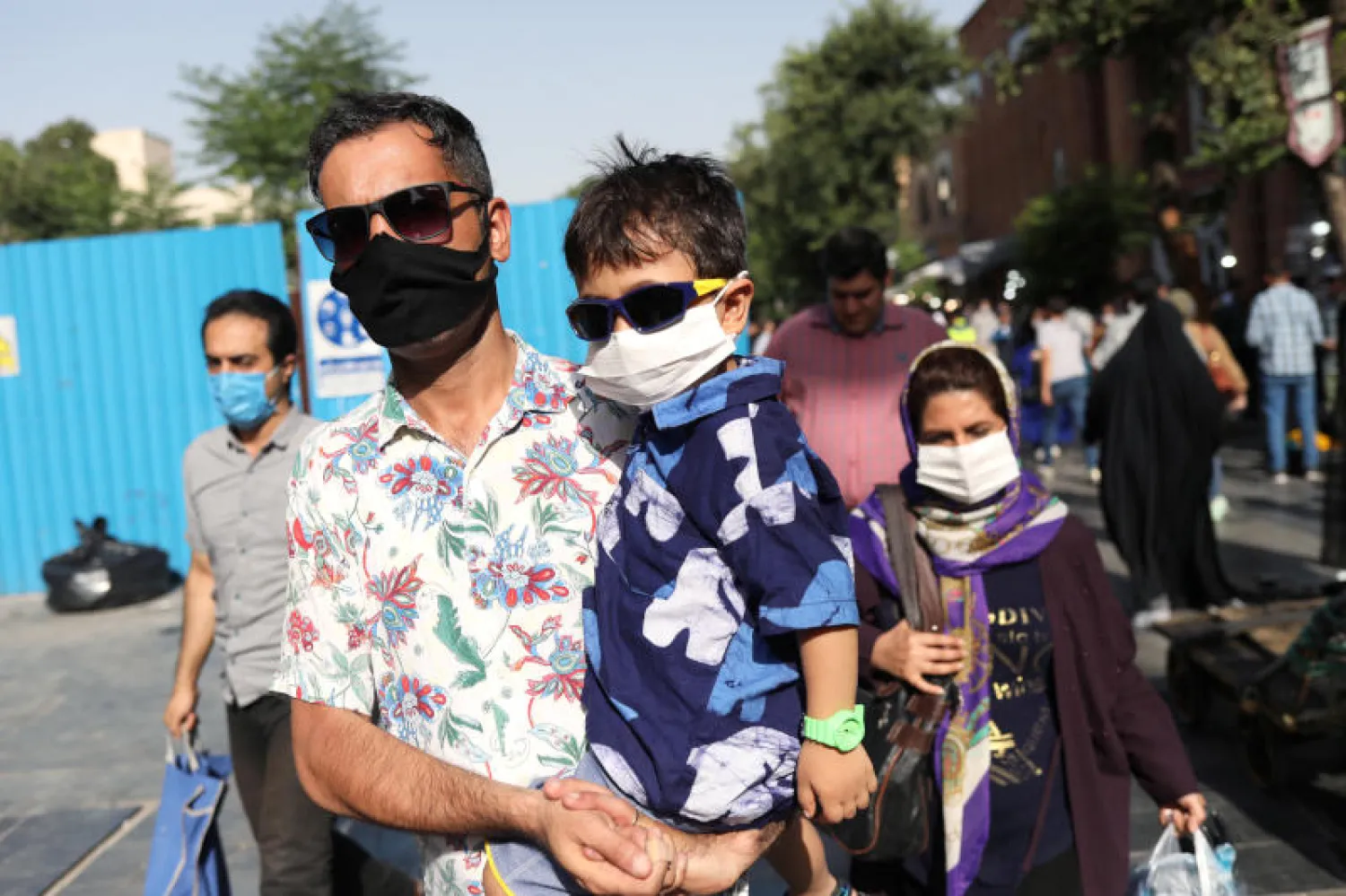 رجل إيراني وابنه يرتديان قناع الوجه الواقي ويمشيان في أحد شوارع طهران (رويترز)