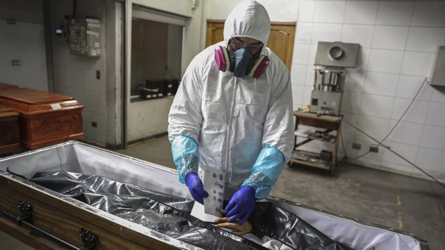 An employee takes the fingerprints of a woman who died from the new coronavirus before her remains are cremated at La Recoleta crematorium in Santiago, Chile, Saturday, June 27, 2020. (AP Photo/Esteban Felix)