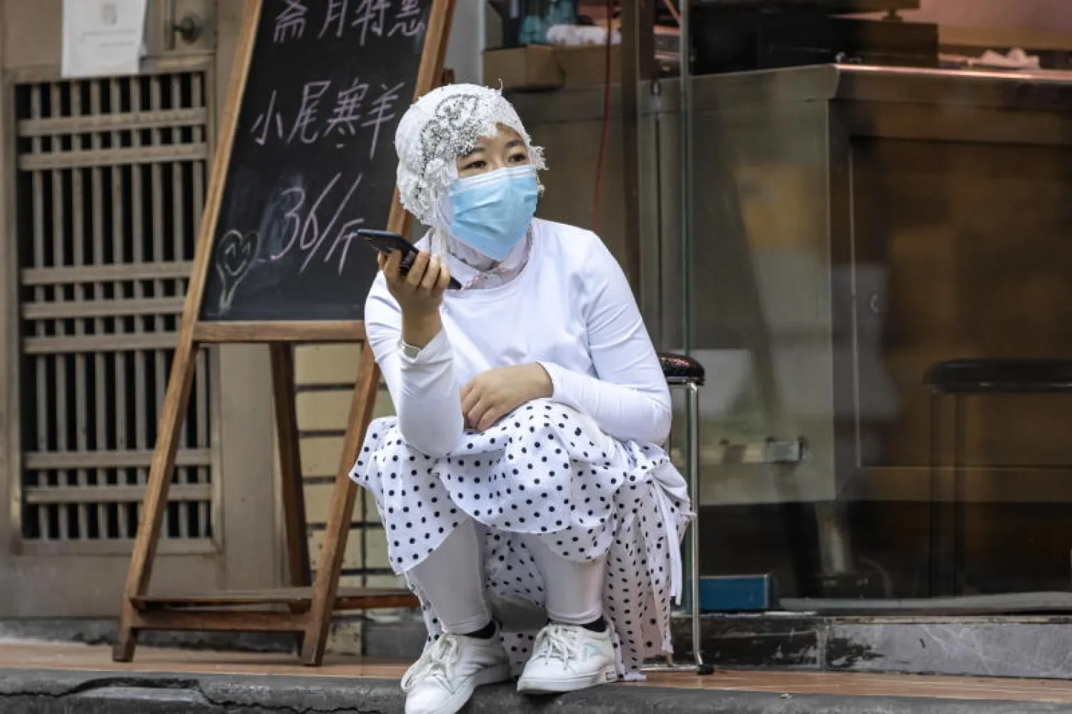 امرأة تنتمي لأقلية الأويغور المسلمة تجلس أمام متجرها بمقاطعة غوانغدونغ بالصين (إ.ب.أ)