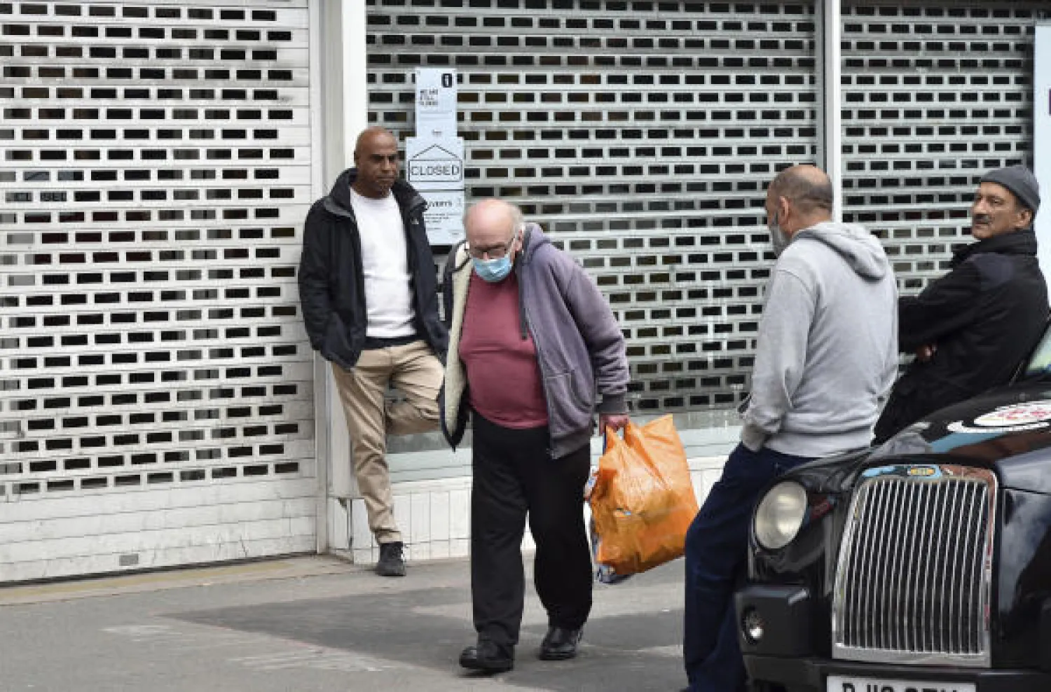People stand outside a closed shop in Leicester city centre, England, Tuesday June 30, 2020. The British government has reimposed lockdown restrictions in the English city of Leicester after a spike in coronavirus infections, including the closure of shops that don't sell essential goods and schools. (AP Photo/Rui Vieira)
