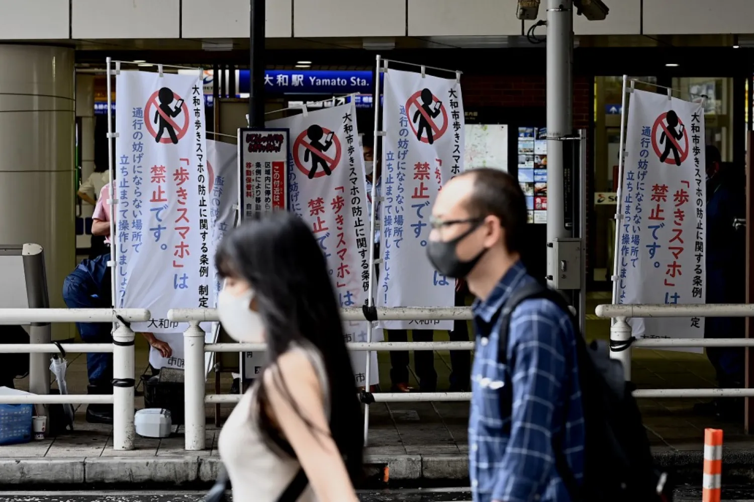 People walk past banners installed by the city hall to inform pedestrians about the ban on using a mobile phone while walking, in Yamato, Kanagawa prefecture on July 1, 2020. (AFP)