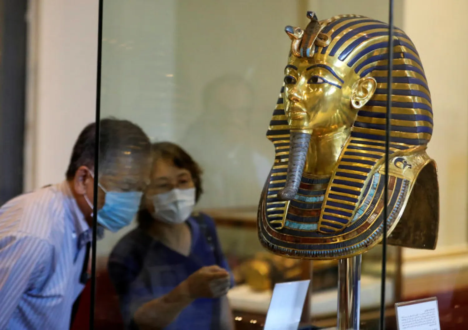 سائحان يضعان كمامتين وينظران إلى القناع الذهبي لتوت عنخ آمون في المتحف المصري (رويترز)