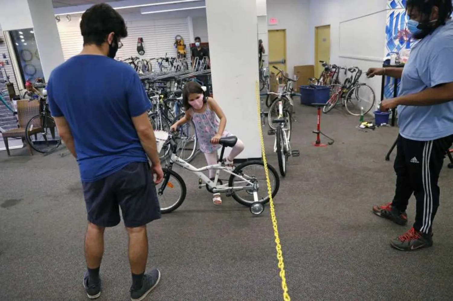 In this Wednesday, June 24, 2020, photograph, Mahdi Hashemian, of Cambridge, Mass., left, watches as his daughter Zeynab climbs onto her first bicycle as technician Dell Wilkerson Jr. looks on at Spokehouse Bikes in the Upham's Corner neighborhood of Boston. Hashemian decided to buy his daughter's bike at the store to support the Black-owned business, which was robbed and vandalized earlier in the month. (AP Photo/Charles Krupa)