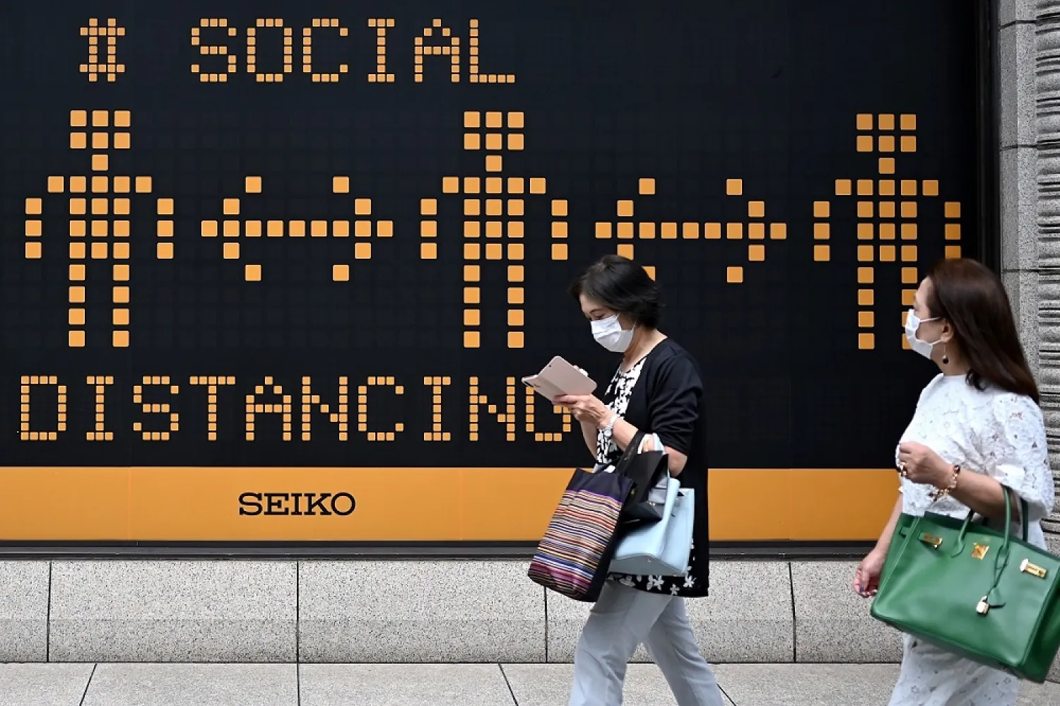 Masked pedestrians walk past a billboard reminding people on social distancing practices amid the COVID-19 coronavirus pandemic in Tokyo. (AFP)