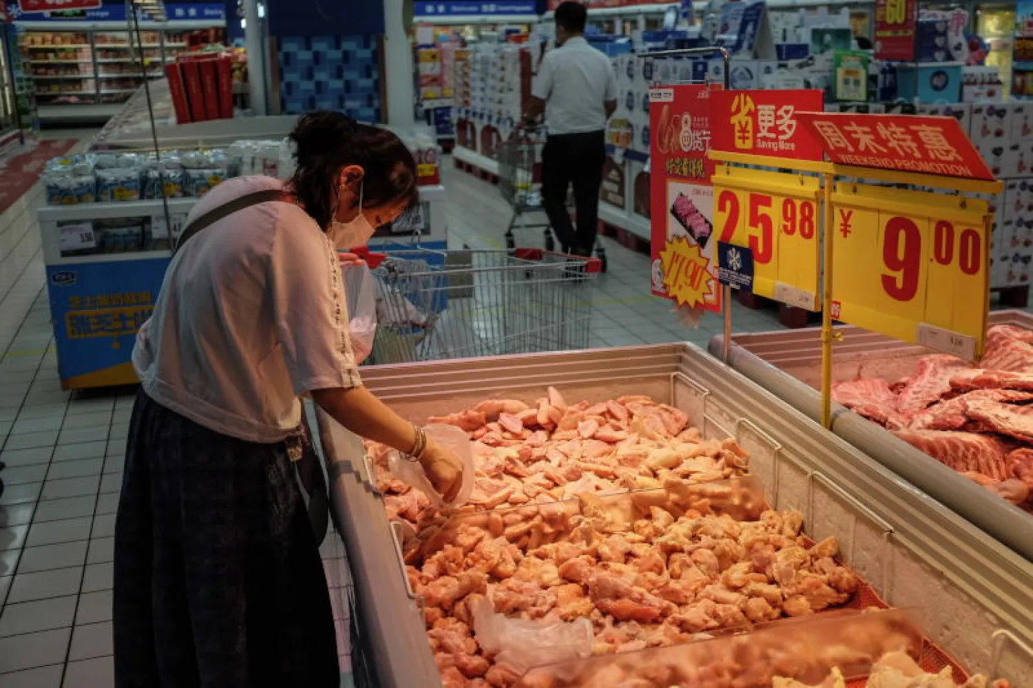 سيدة ترتدي قناعا واقيا تفحص مجموعة من الدجاج في أحد أسواق بكين (إ.ب.أ)