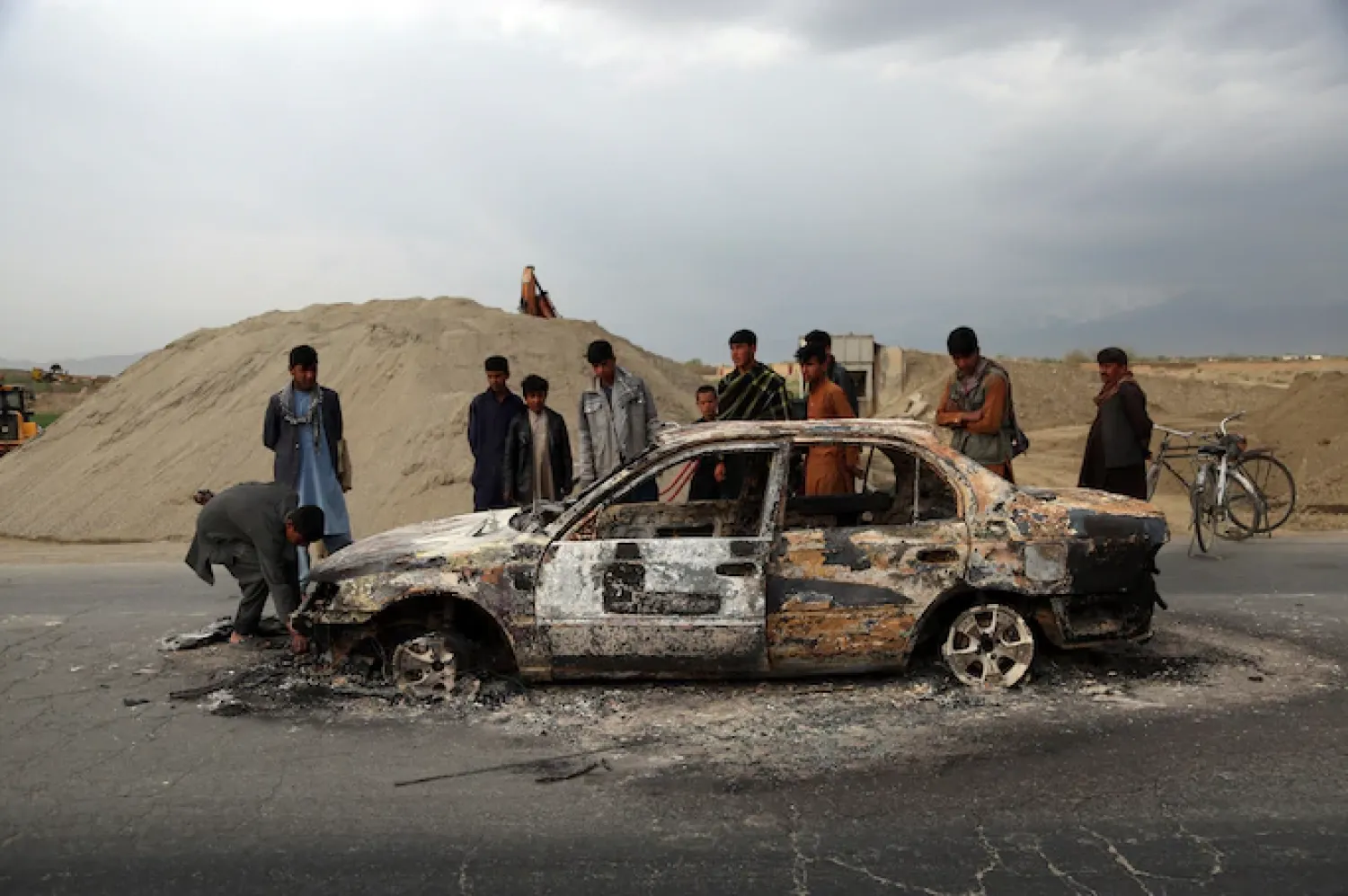 FILE - In this April 9, 2019, file photo, Afghans watch a civilian vehicle burnt after being shot by U.S. forces following an attack near the Bagram Air Base, north of Kabul, Afghanistan. Three American service members and a U.S. contractor were killed when their convoy hit a roadside bomb on Monday near the main U.S. base in Afghanistan, the U.S. forces said. The Taliban claimed responsibility for the attack. Intelligence alleging that Afghan militants might have accepted Russian bounties for killing American troops didn’t scuttle the U.S.-Taliban agreement or President Donald Trump’s plan to withdraw thousands more troops from the war. (Rahmat Gul, File/Associated Press)
