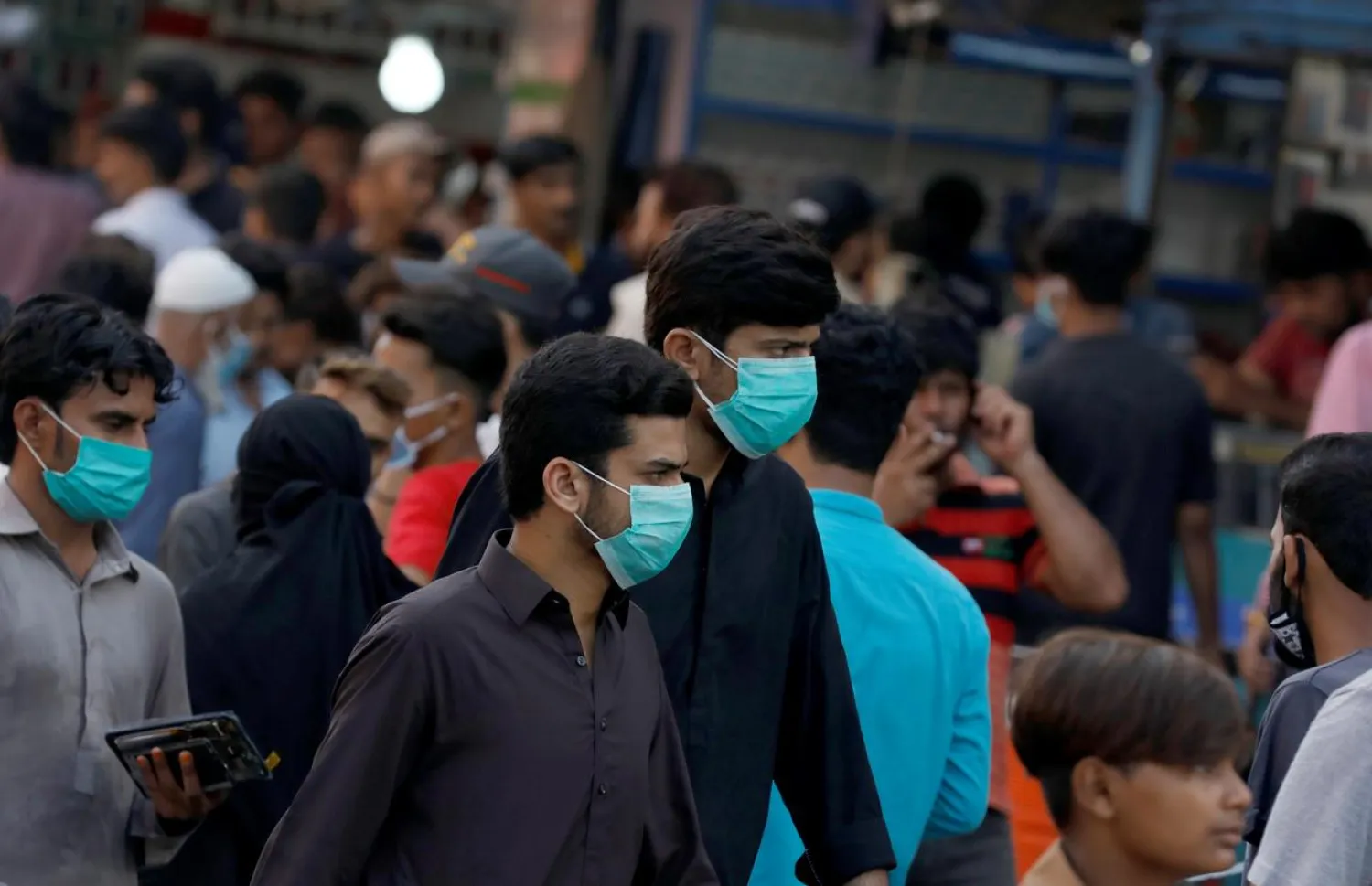 Men wearing protective face masks walk amid the rush of people outside a market as the outbreak of the coronavirus continues, in Karachi, Pakistan June 8, 2020. (Reuters)