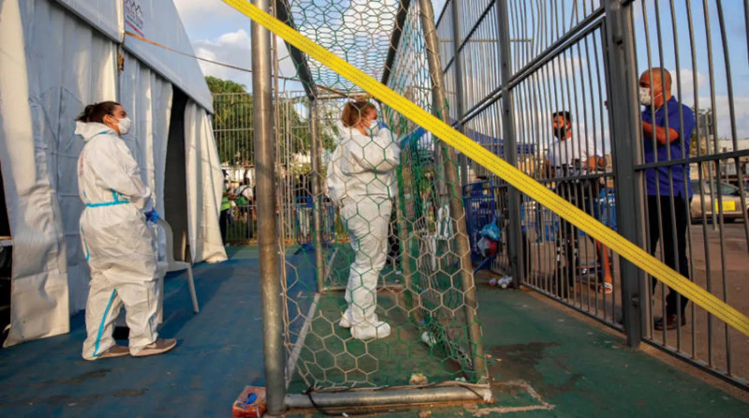 عمال صحة إسرائيليون يتحدثون مع رجل يريد فحص نفسه من {كورونا} في مركز بتل أبيب (أ.ب)