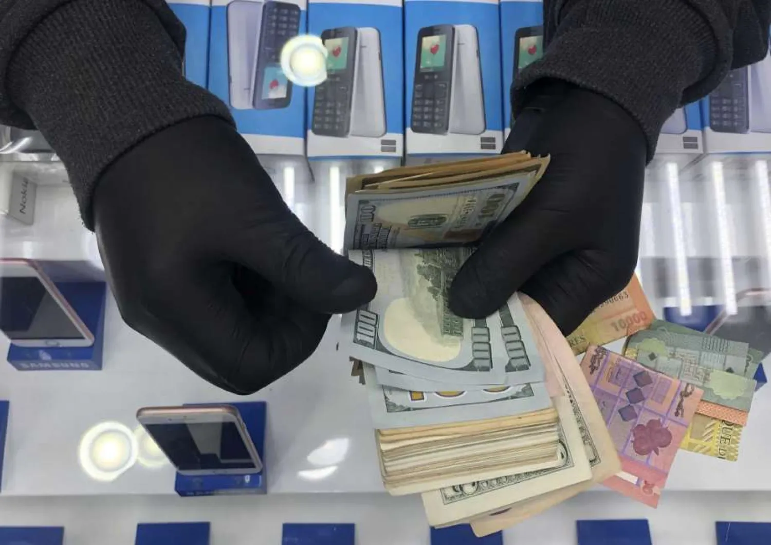 In this April 28, 2020 file photo, a cell phone shop owner wears gloves as he counts US dollars, in Beirut, Lebanon. (AP Photo/Hussein Malla, File)