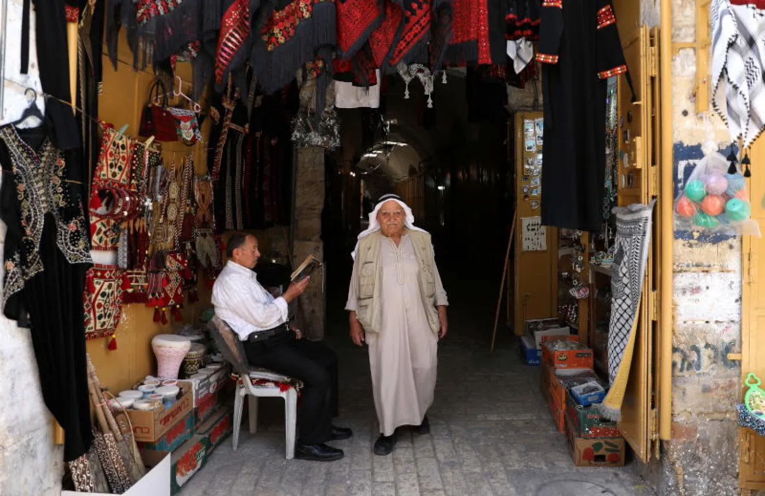 رجل يمشي وآخر يجلس في البلدة القديمة بمدينة الخليل بالضفة الغربية (إ.ب.أ)