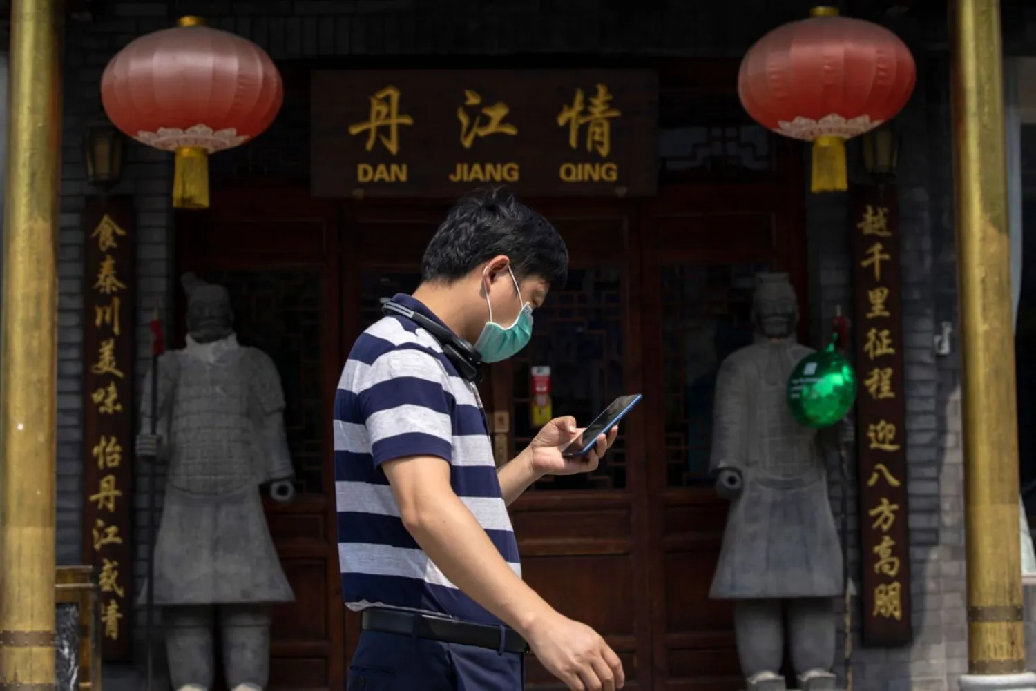 A man wearing a mask to curb the spread of the coronavirus walks past replicas of the Terracotta Warriors outside a restaurant in Beijing on Wednesday, July 8, 2020. (AP Photo/Ng Han Guan)