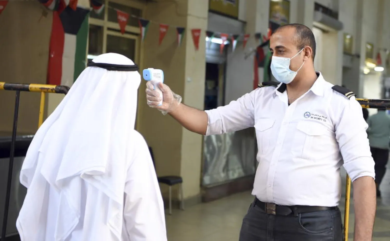 رجل أمن يفحص درجة حرارة أحد العملاء عند مدخل مركز للتسوق في مدينة الكويت (إ.ب.أ)