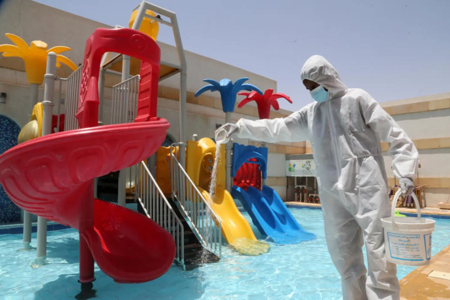 عامل يرتدي بذلة واقية ويعقم حوض الشاليه قبل أن تستأجره عائلات سعودية في الرياض (رويترز)