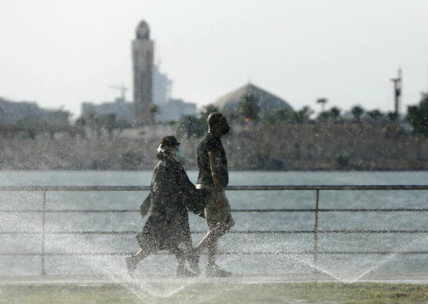 المصطافون يمشون وهم يرتدون أقنعة واقية للوجه على شاطئ البحر الأحمر في جدة (أ.ب)