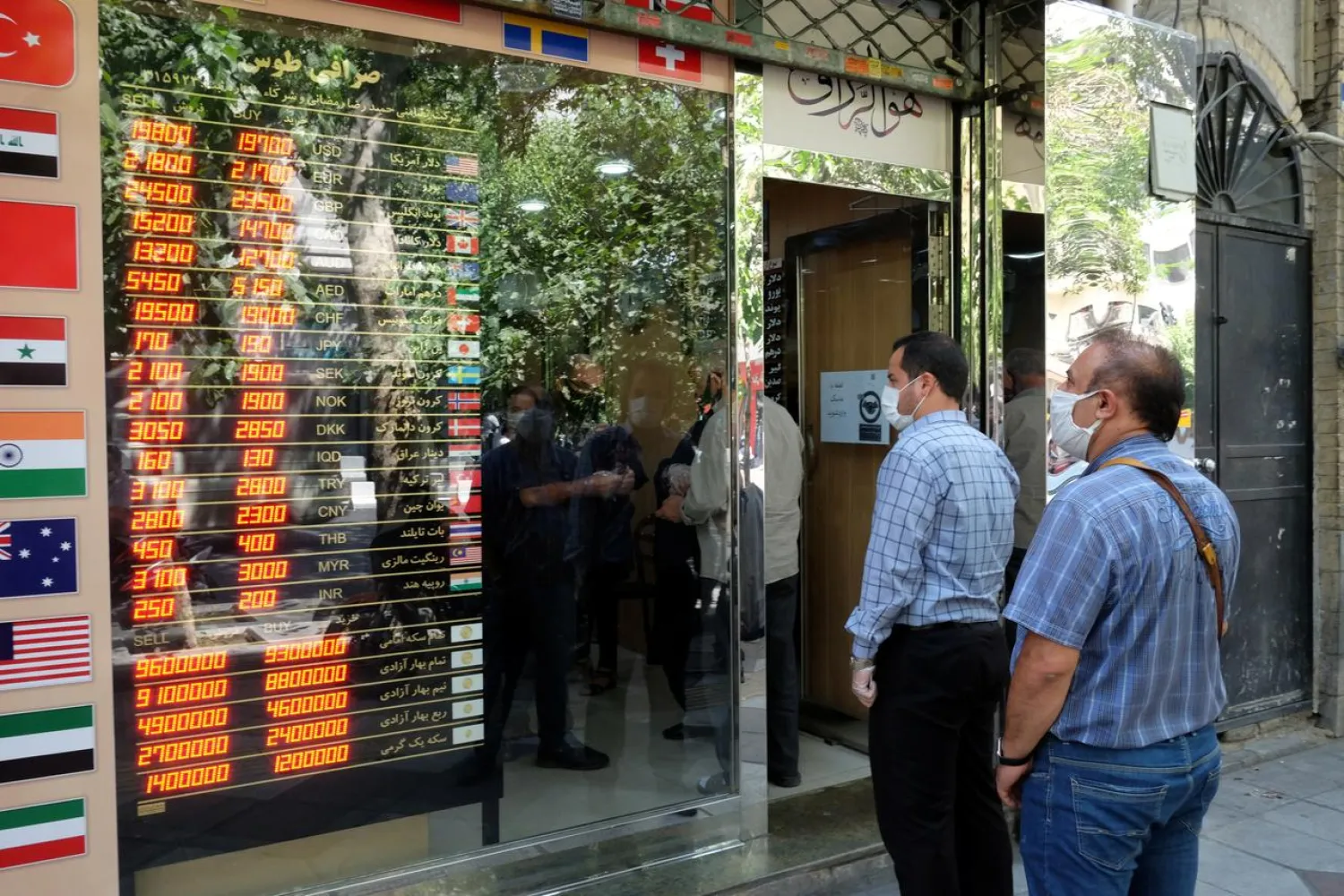 People wear protective face masks as they look at the electronic currency board at Ferdowsi square in Tehran, Iran July 2, 2020. (Reuters)